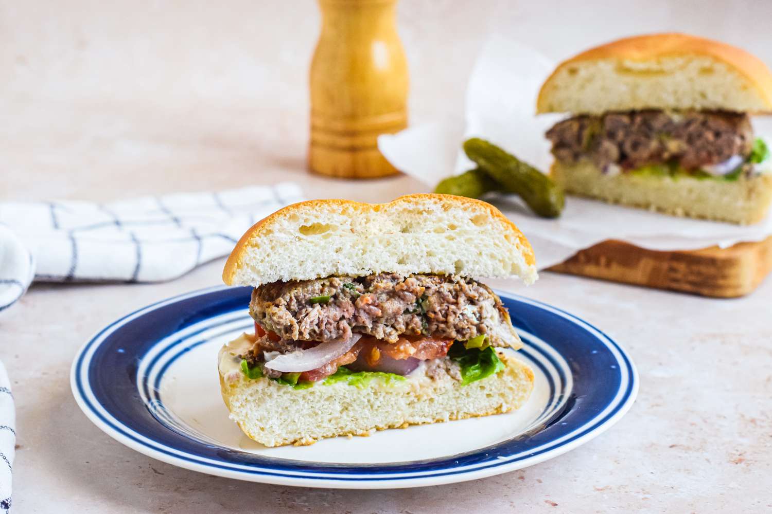 A Plate with a Blue Cheese Burger Cut in Half and in the Background, the Other Half of the Burger Is on Parchment Paper with Pickles
