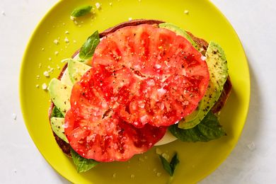Open-faced sandwich with tomato, avocado, mozzarella, and basil on a yellow plate