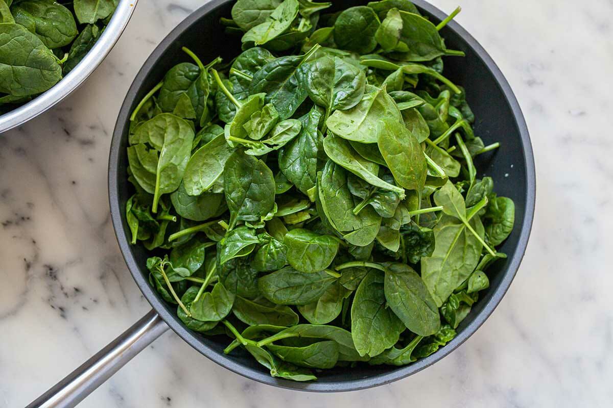 A non-stick skillet filled with fresh spinach to make Spinach in Creamed Mustard Sauce.