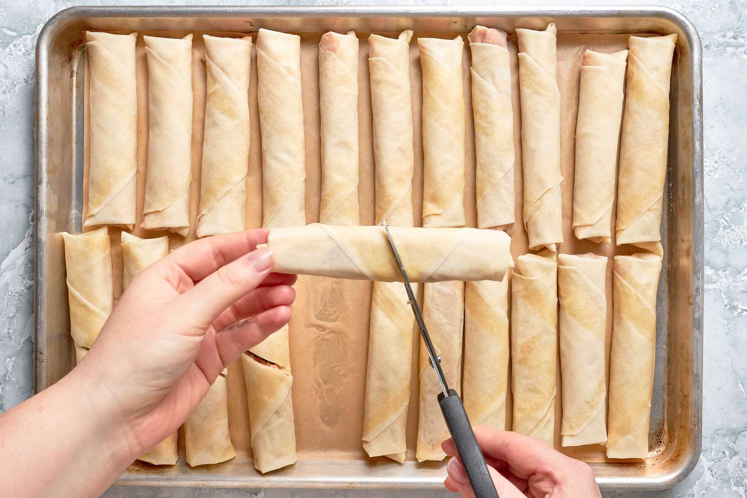 Lumpia Cut in Half Using a Pair of Scissors, and Beneath It, More Lumpia Resting on the Baking Tray