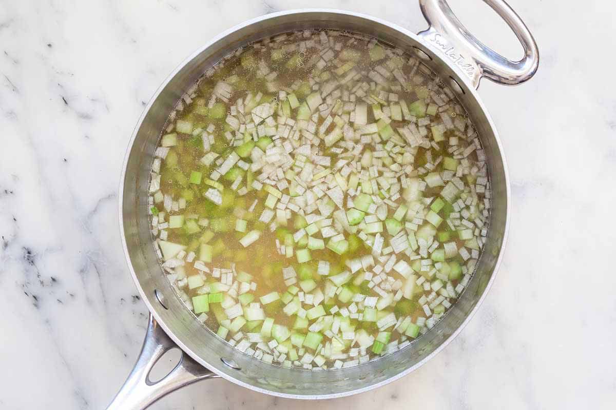 Poaching liquid for chicken in a sauce pot with garlic and onions.