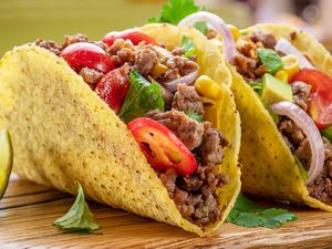 Two tacos on a wooden surface filled with ground beef sliced vegetables and garnishes