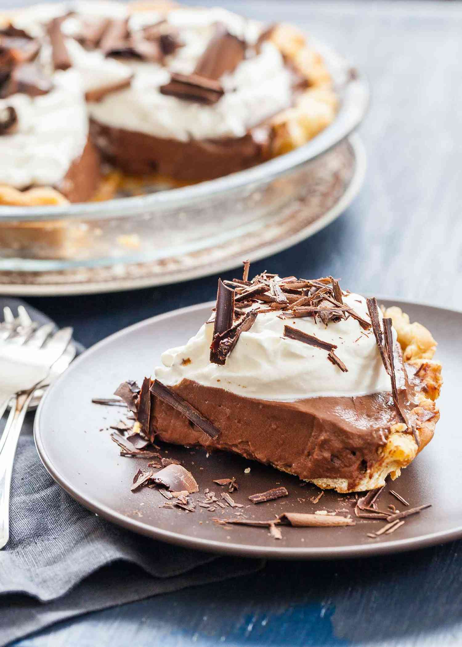 A slice of Chocolate Pudding Pie on a plate with the rest of the pie set behind it.