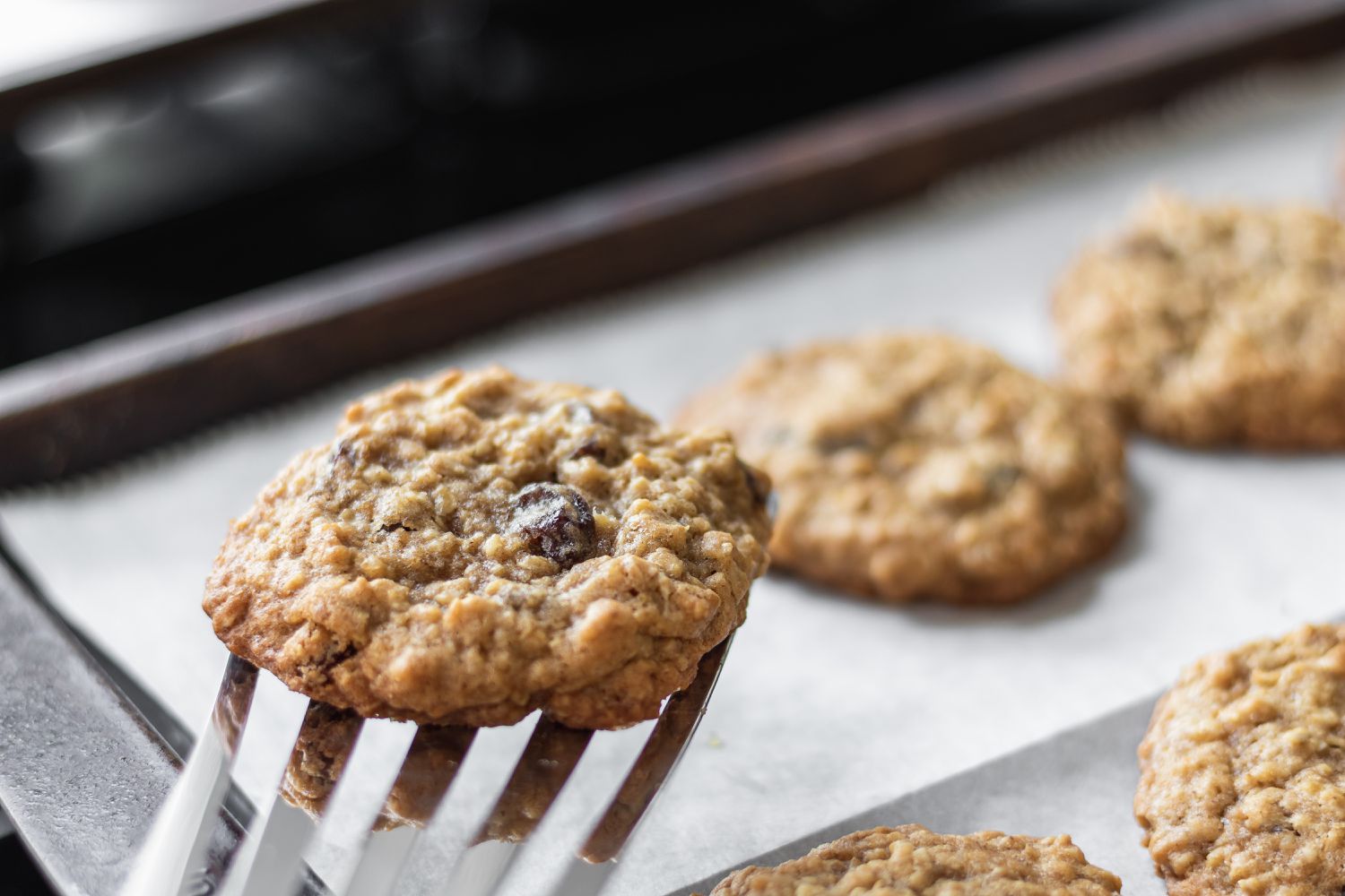 Scooping Oatmeal Raisin Cookies off a baking sheet.