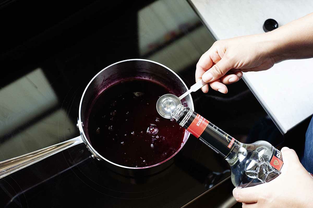 Kirschwasser is being added to cherries cooking on a stove for an Authentic Black Forest Cake.