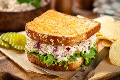 Tuna salad sandwich next to pickles and chips