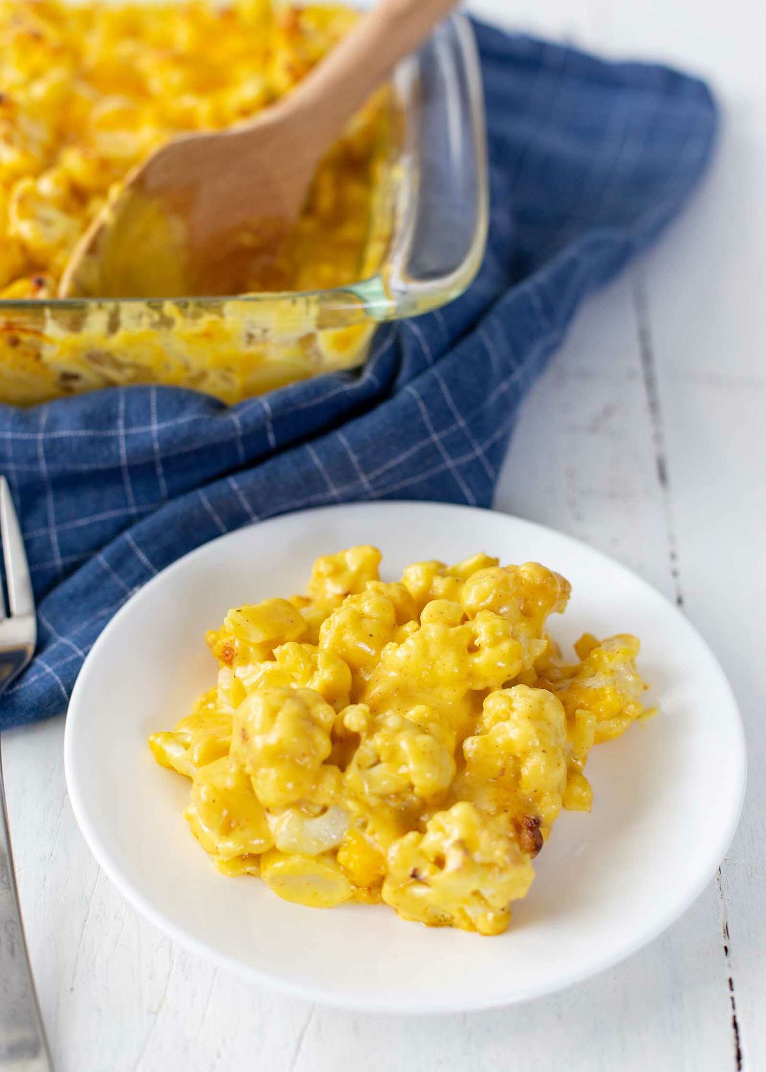 Baked Cheesy Cauliflower scooped on a plate with the casserole dish behind it.