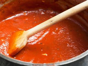 A pot of tomato sauce being stirred with a wooden spoon featured in a reciperelated context