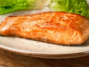 Side view of an oven baked salmon fillet on a pate with lettuce in the background