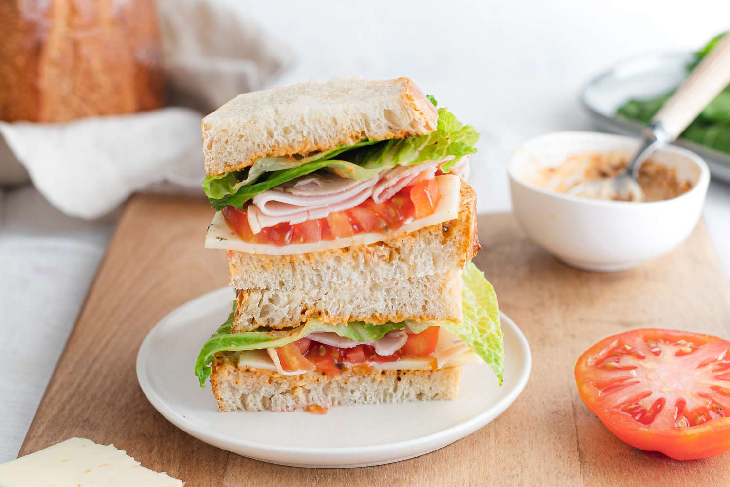 Sandwich Made with Sourdough Sandwich Loaf Slices, Turkey Slices, Tomato Slice, and Lettuce and Stacked on a Cutting Board with the Remaining Ingredients in the Surroundings