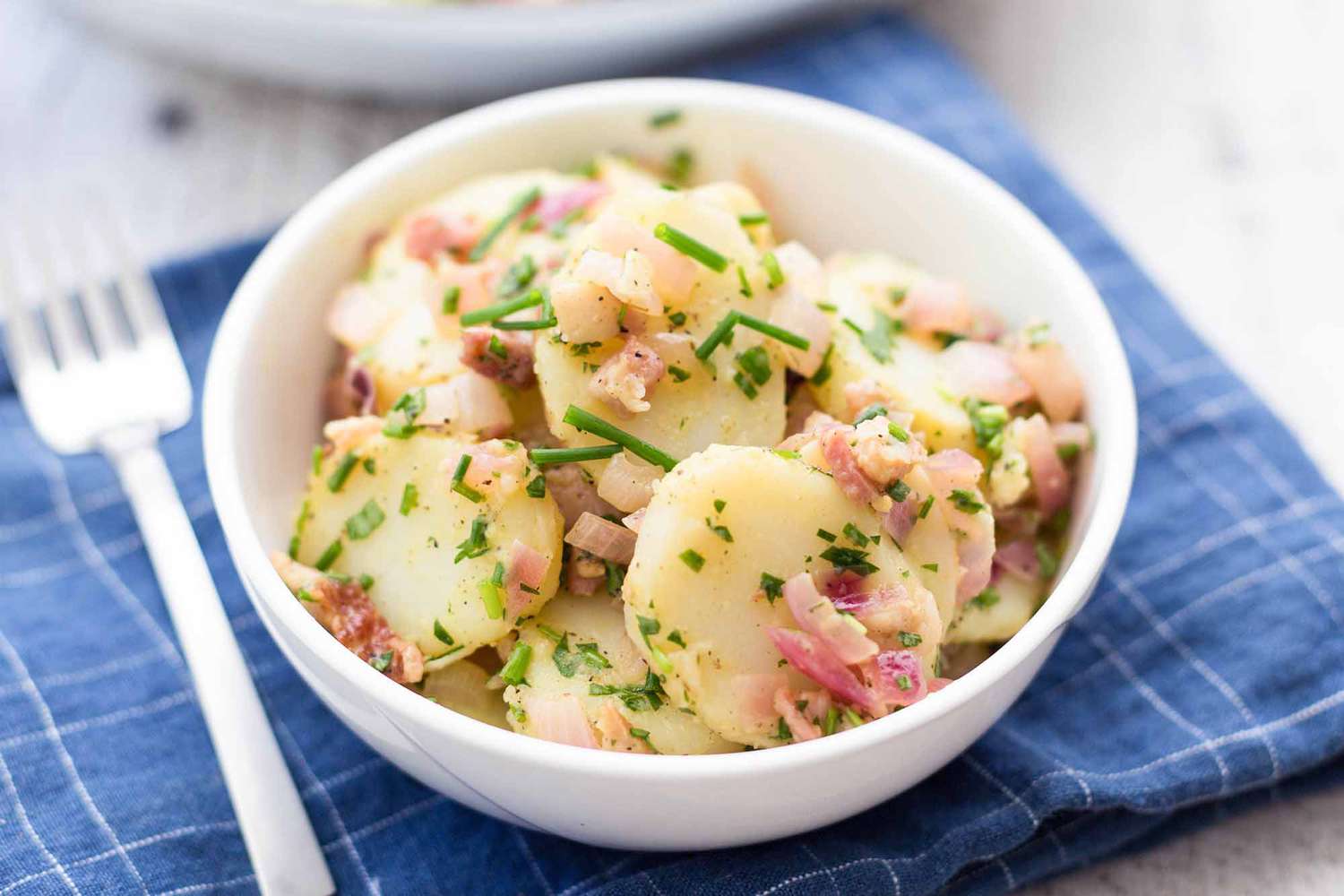 A bowl of potato salad on a blue napkin with a fork, ready to eat