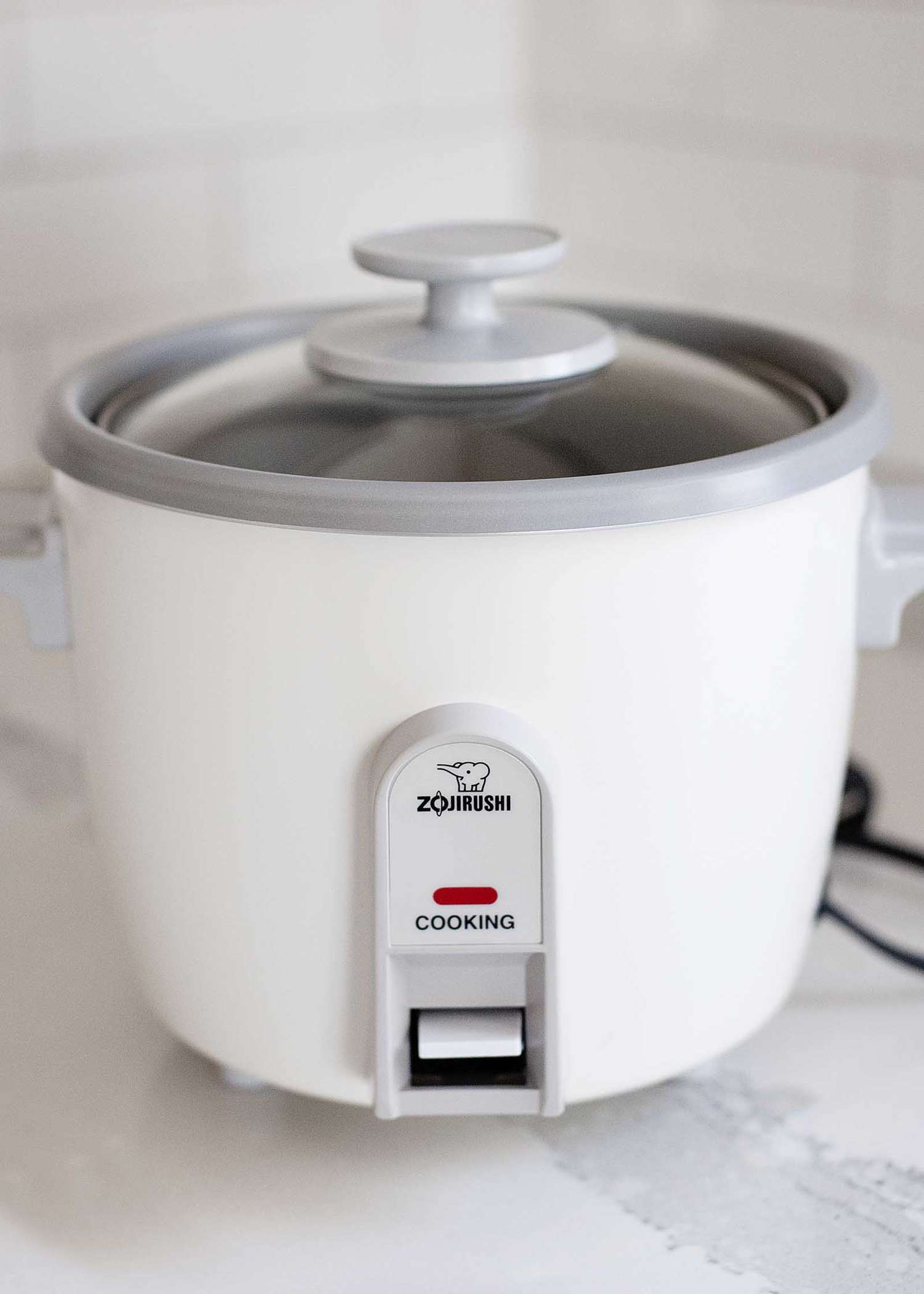 A rice cooker with a glass lid on a countertop