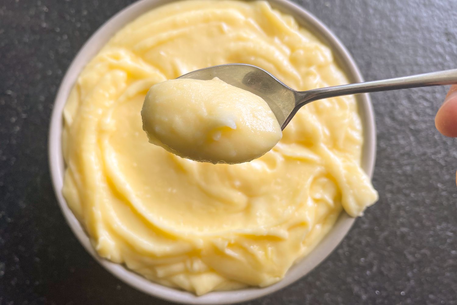 A spoon with mashed potatoes held over a bowl of mashed potatoes