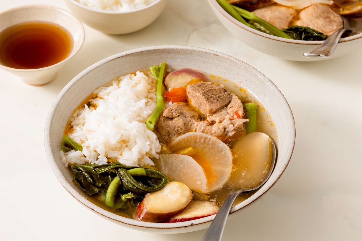 A bowl of pork sinigang with rice and vegetables served with sides of soup and additional rice