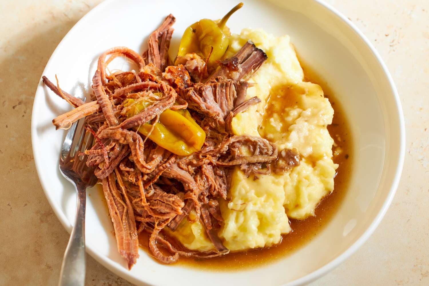 Plate of shredded beef mashed potatoes and pepperoncini with gravy meal setting