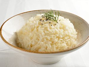 A bowl of cooked jasmine rice garnished with sesame seeds and a sprig of dill