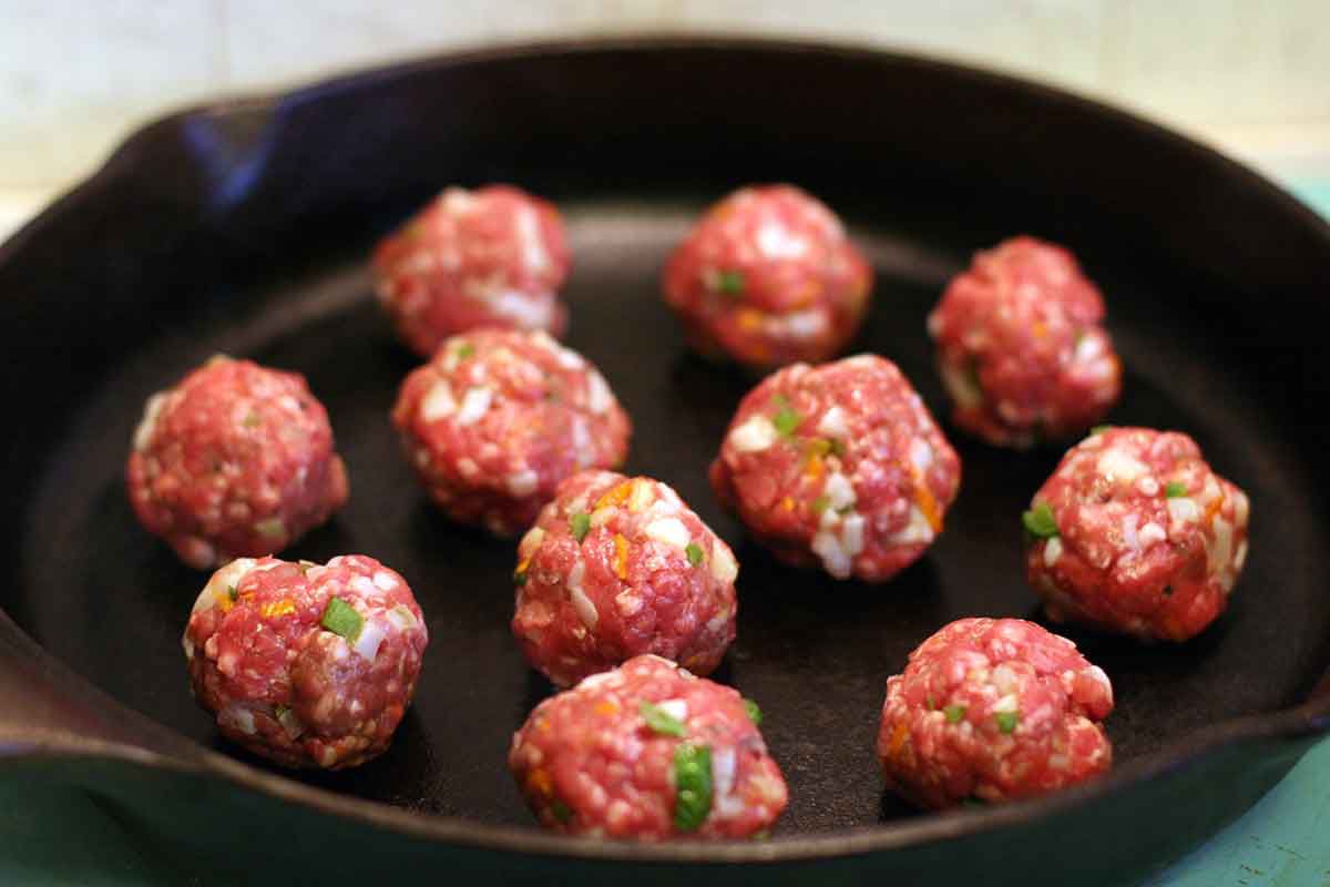 raw greek meetballs cooking in cast iron frying pan