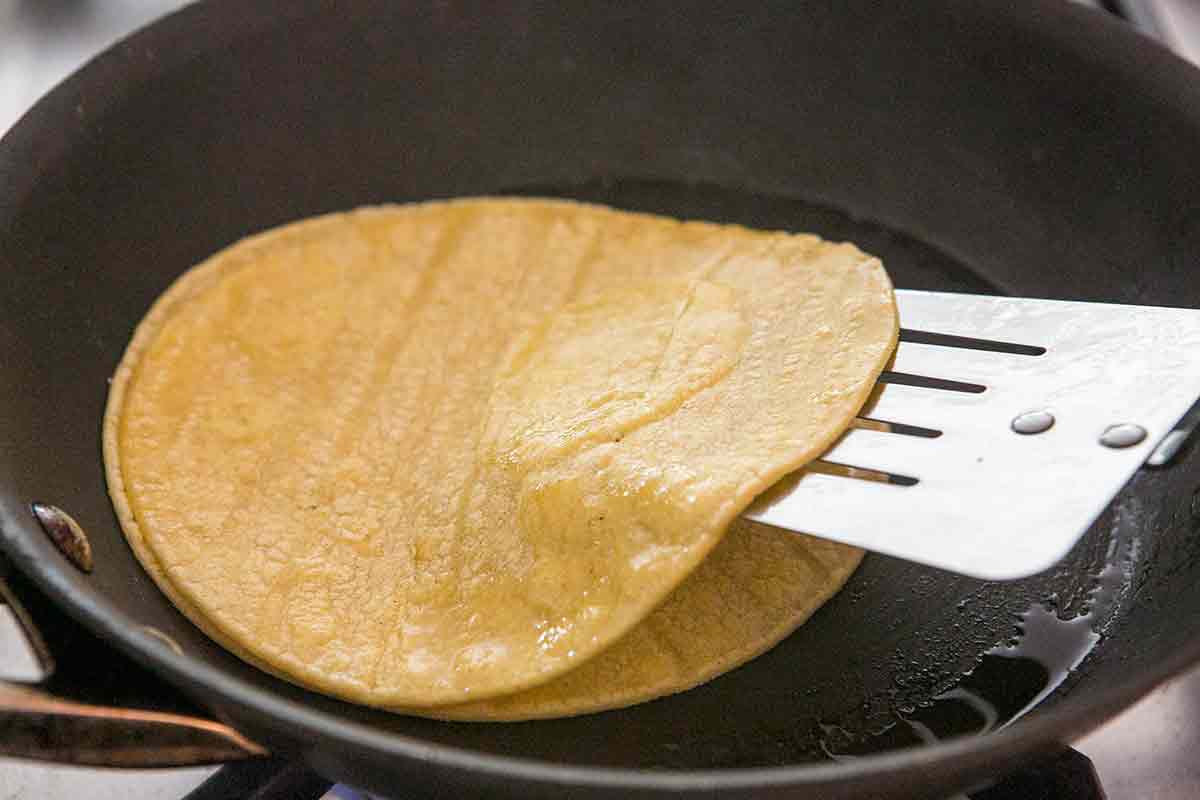 Stack corn tortillas to absorb excess oil for homemade chicken enchiladas