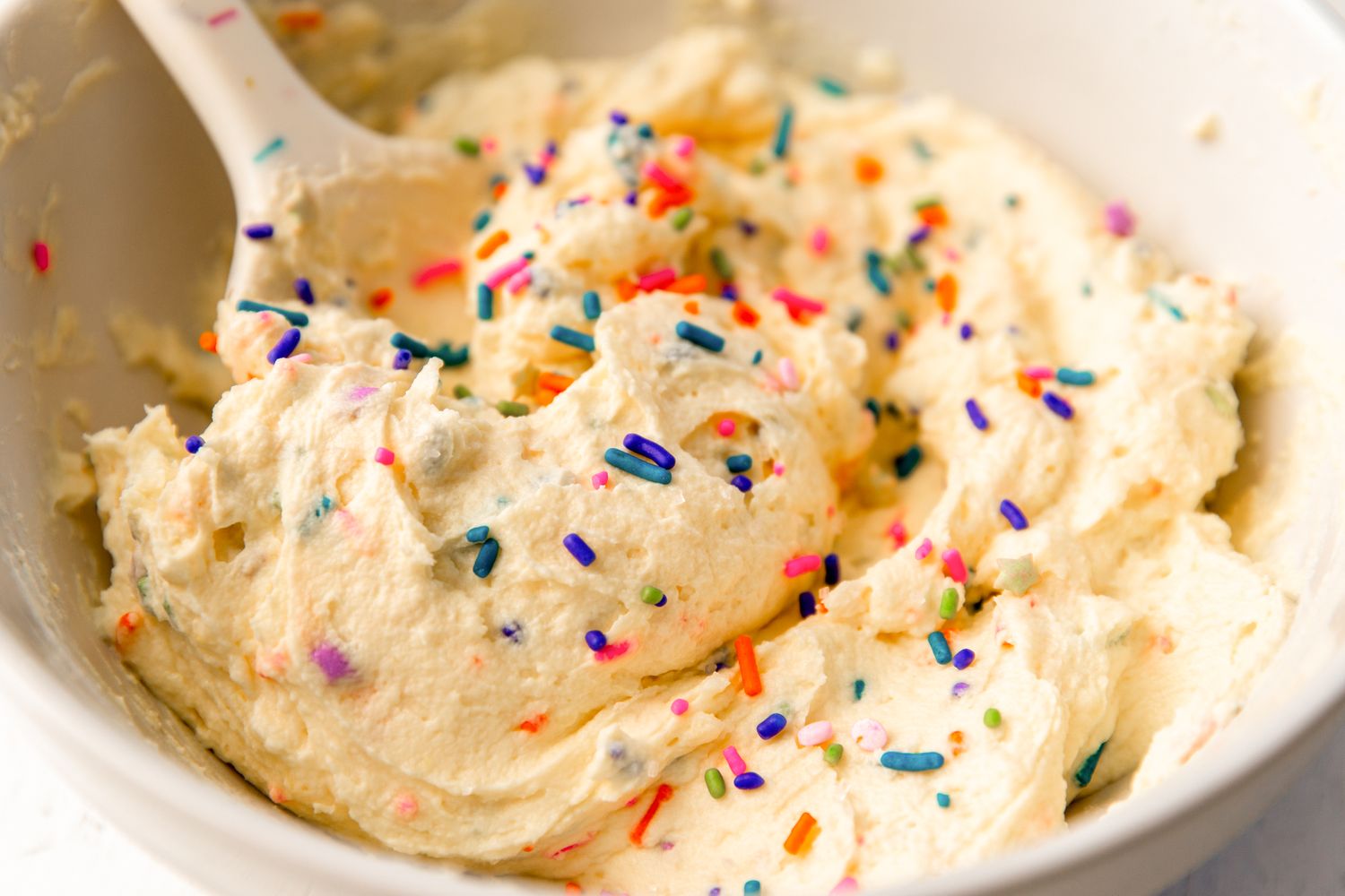 Bowl of frosting with colorful sprinkles and a spoon