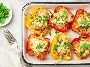 A dish of stuffed bell peppers topped with melted cheese and parsley garnish on a tray served with a fork and parsley on the side