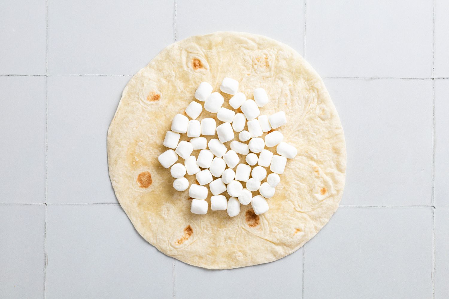 Mini Marshmallows Added to Tortilla on a Counter for S'mores Crunchwrap Recipe
