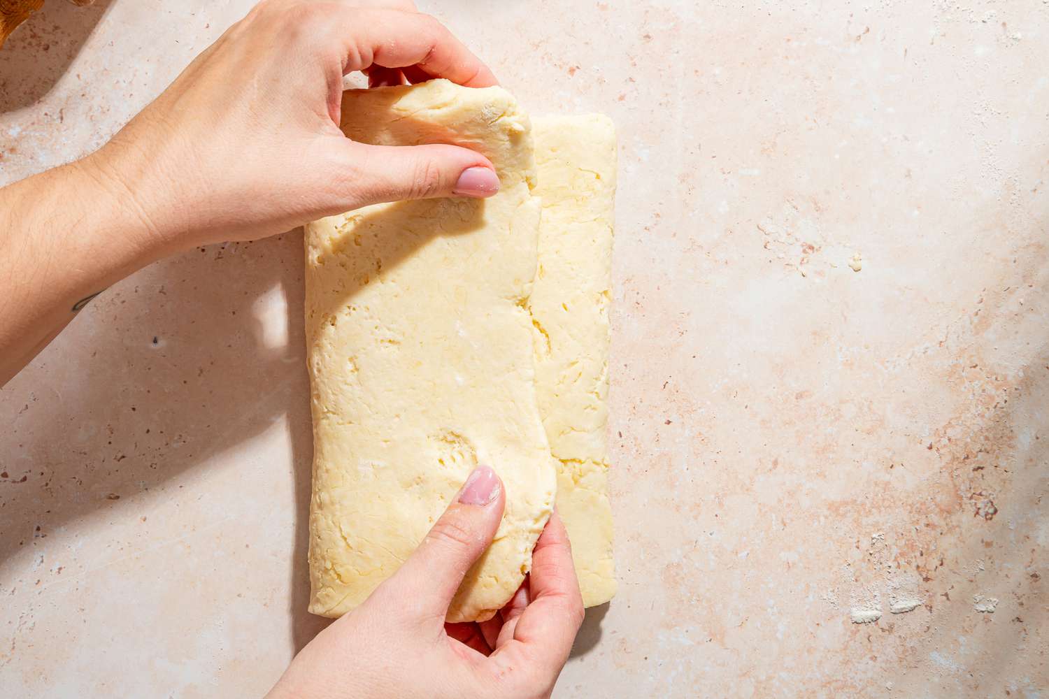 Overhead view of the dough rolled and two hands folding the final fold of dough over for Mayonnaise Biscuits recipe