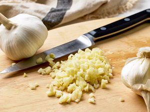 A cutting board with minced garlic a knife and whole garlic bulbs