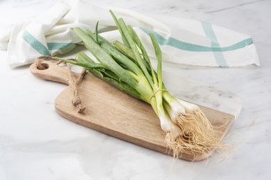 Bunch of green onions with roots on a wooden cutting board