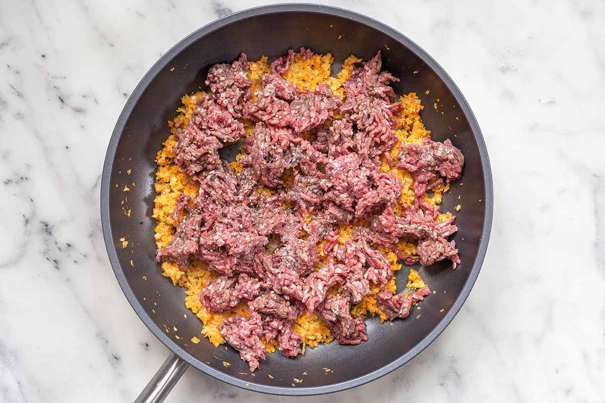 Ground beef and soffritto combined to make fast and easy bolognese sauce in a dark skillet.