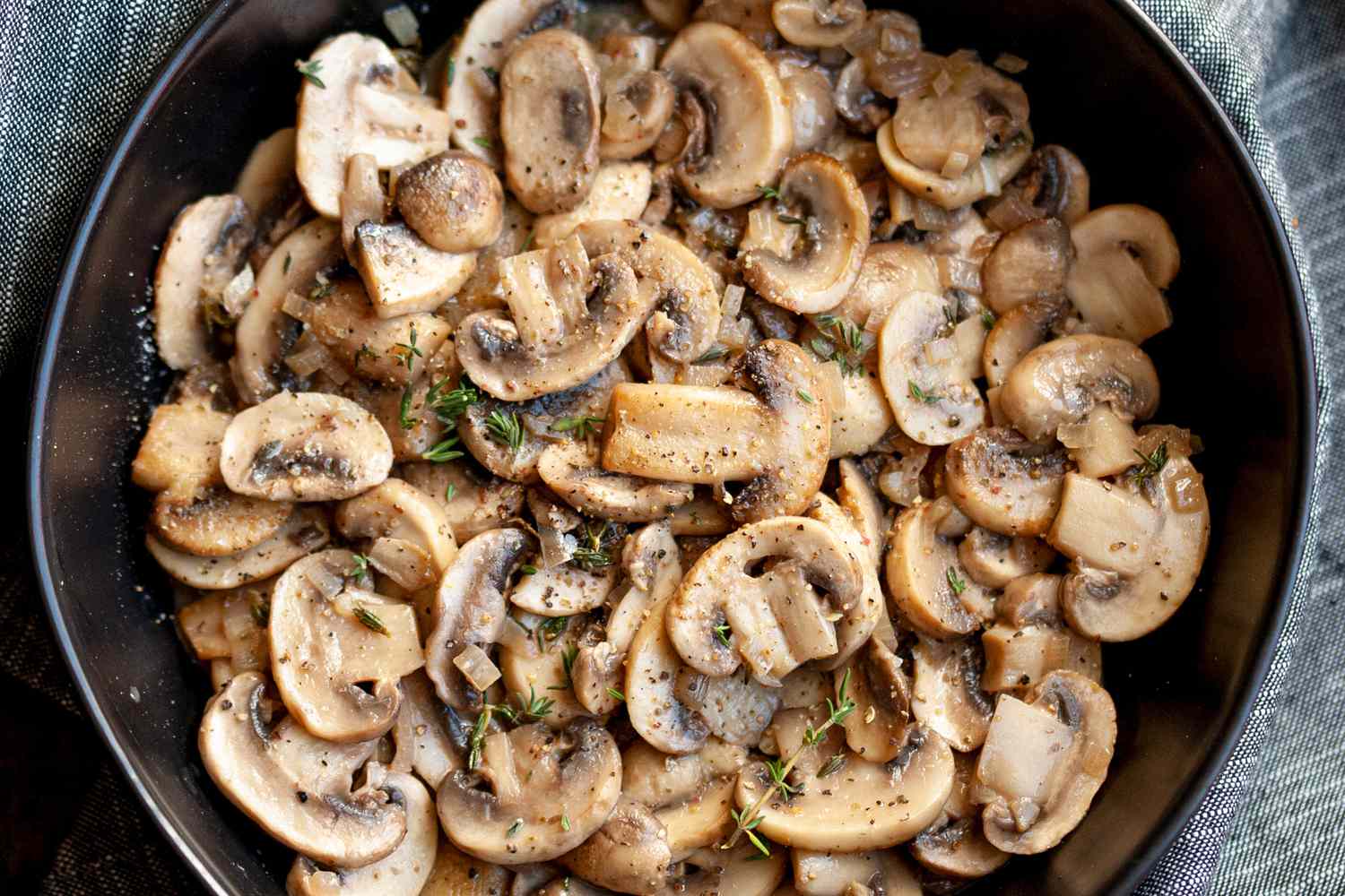 A bowl of sauteed mushrooms garnished with flecks of fresh thyme leaves