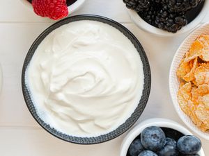 A bowl filled with yogurt next to other bowls with berries and corn flakes