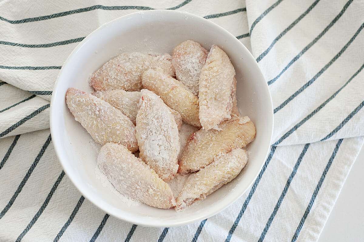 Chicken wings in dusted in baking soda in a white bowl sitting on top of a stripped cloth.