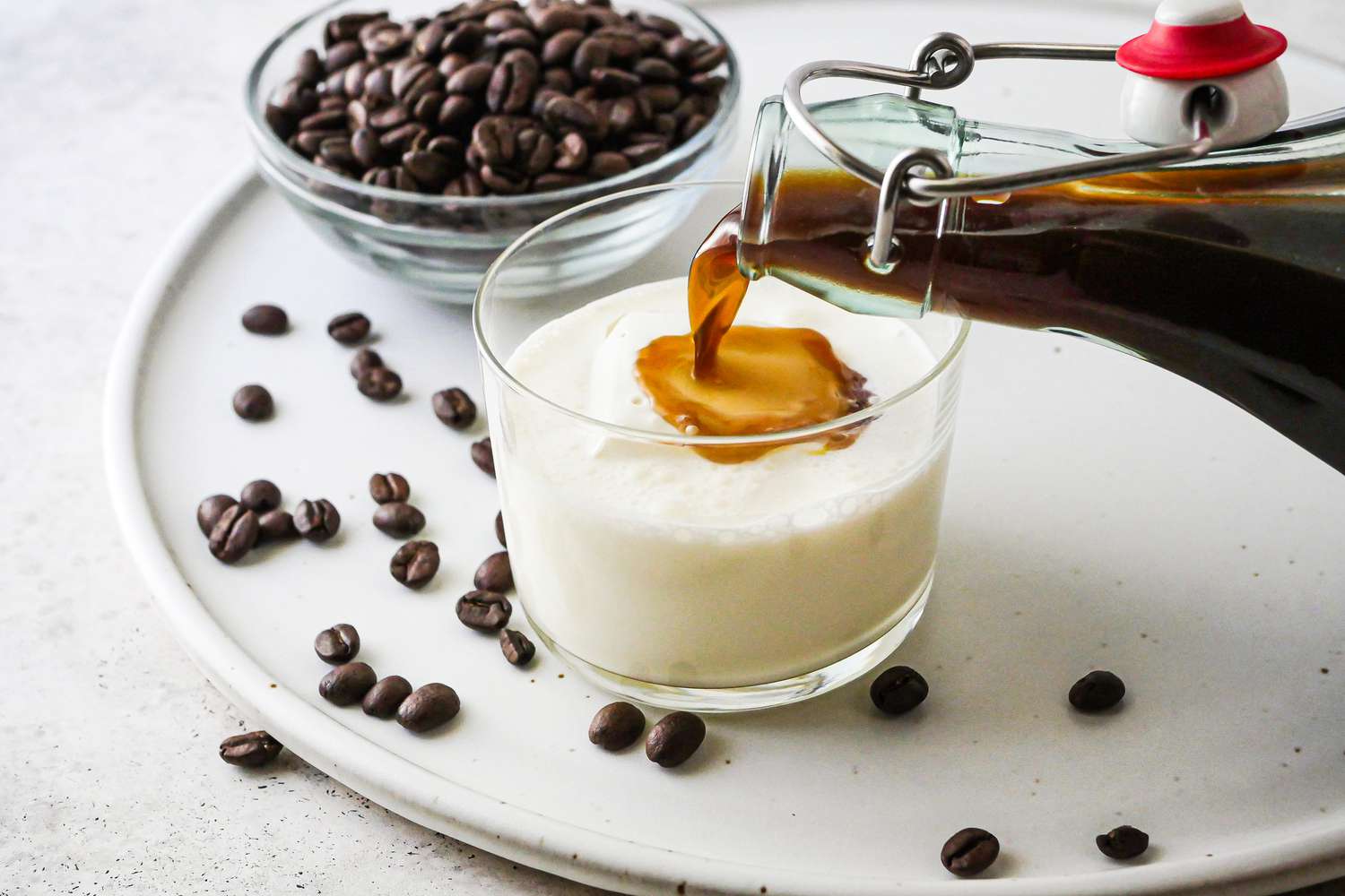 Pouring Vegan Coffee Liqueur in a cocktail glass filled with milk.