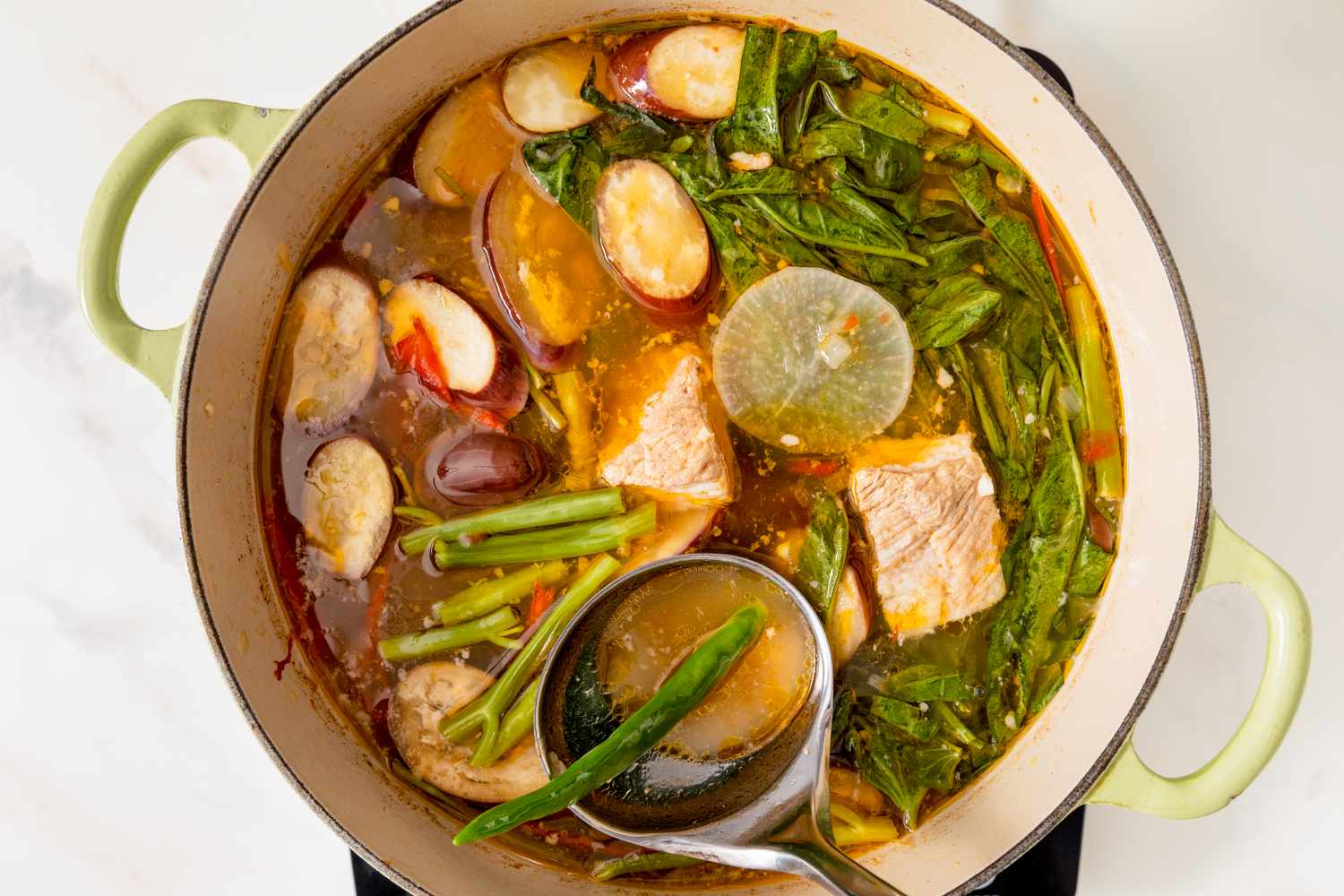 A pot of pork sinigang soup with vegetables like radish and green beans viewed from above