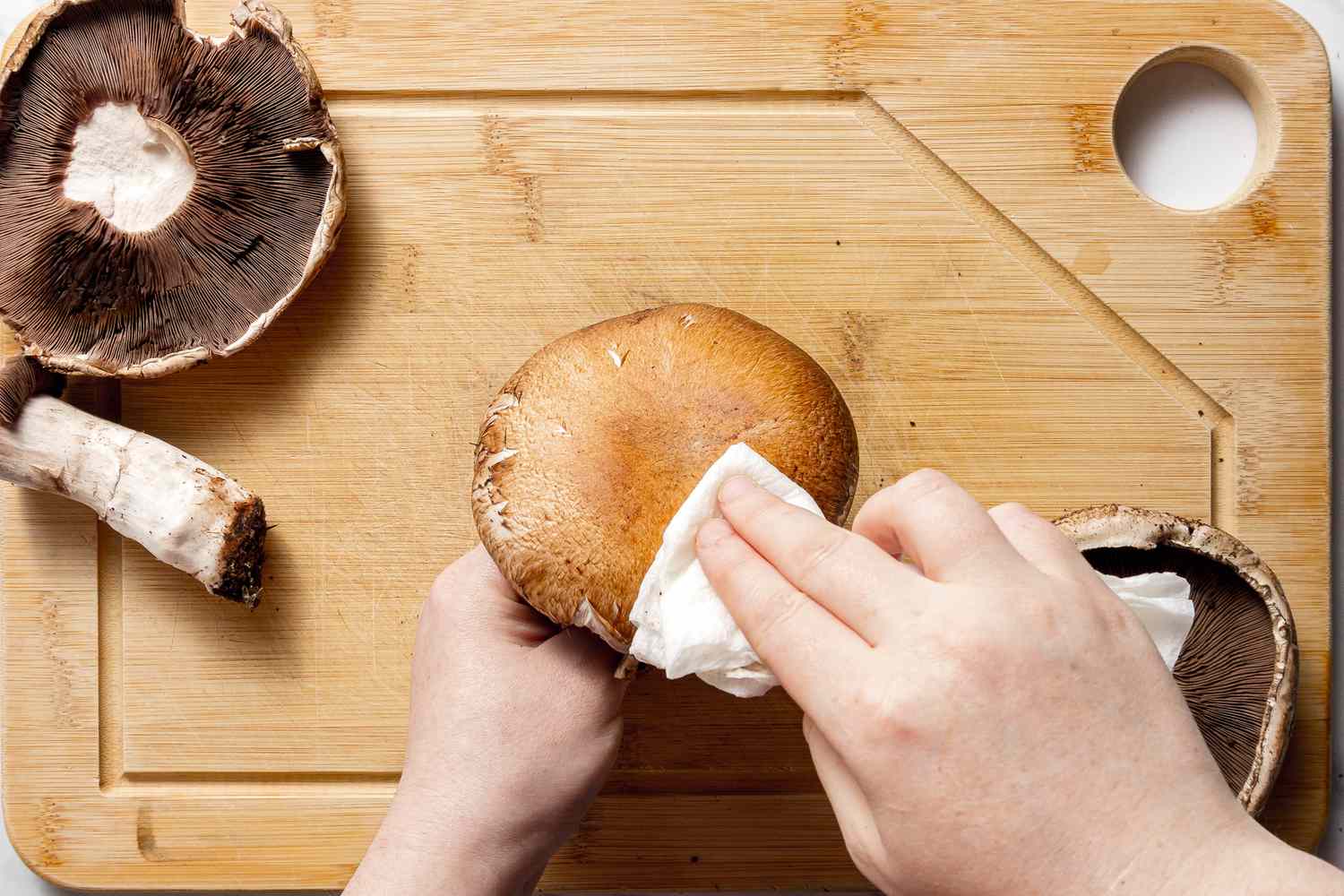 Portobello Mushroom Tops Cleaned on a Cutting Board Using a Wet Paper Towel