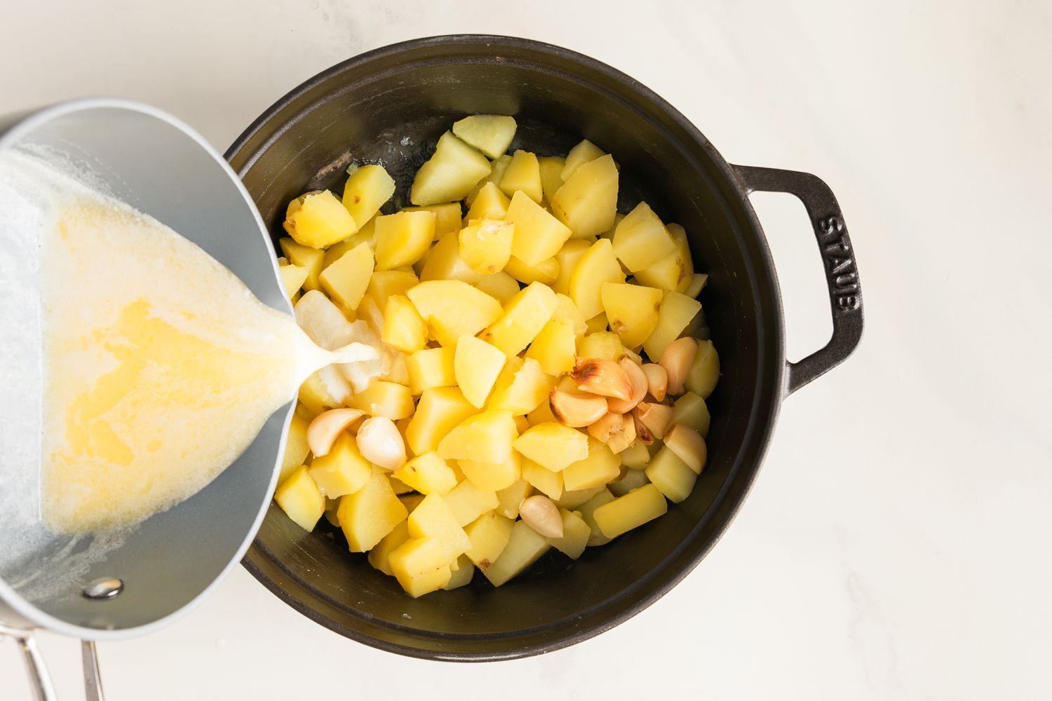 Warm milk and butter being poured over cooked potatoes and roasted garlic