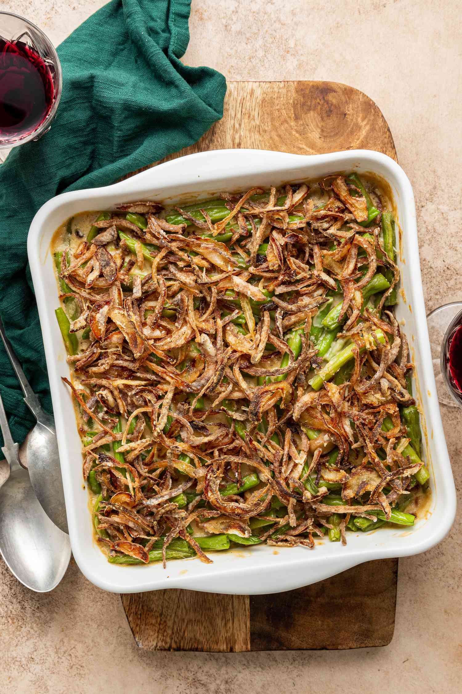 Casserole Dish of Vegan Green Bean Casserole on a Wooden Board, and Next to a Table Napkin, Two Glasses of Wine, and Two Spoons