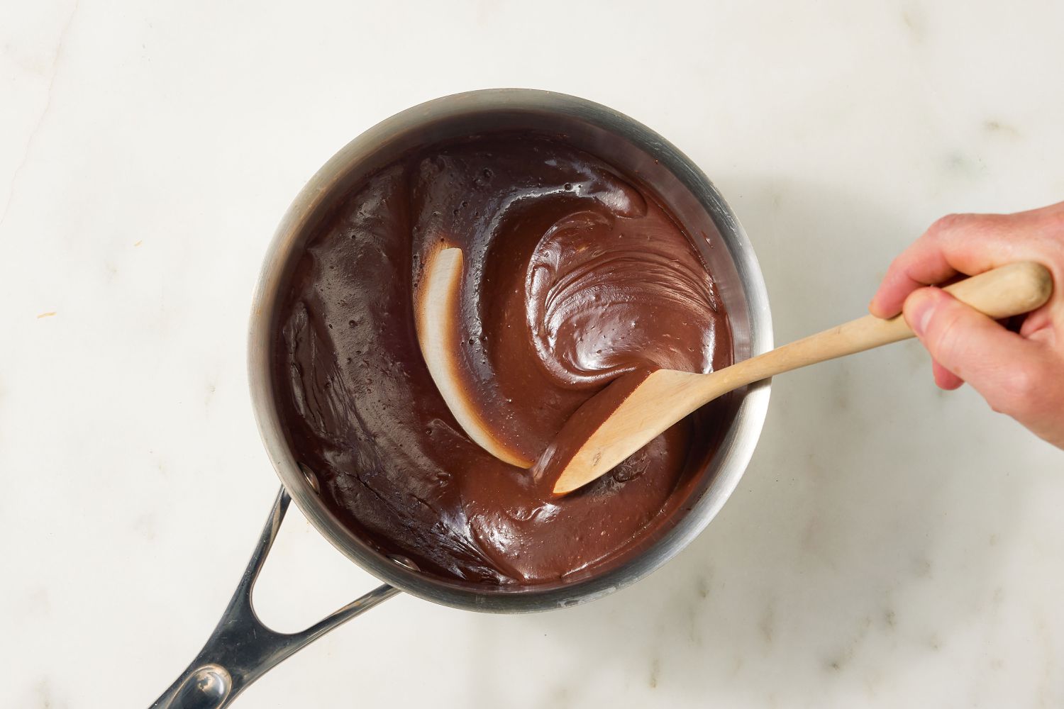 overhead view of chocolate frosting mixture, hand stirring with a wooden spoon - Brazilian Carrot Cake