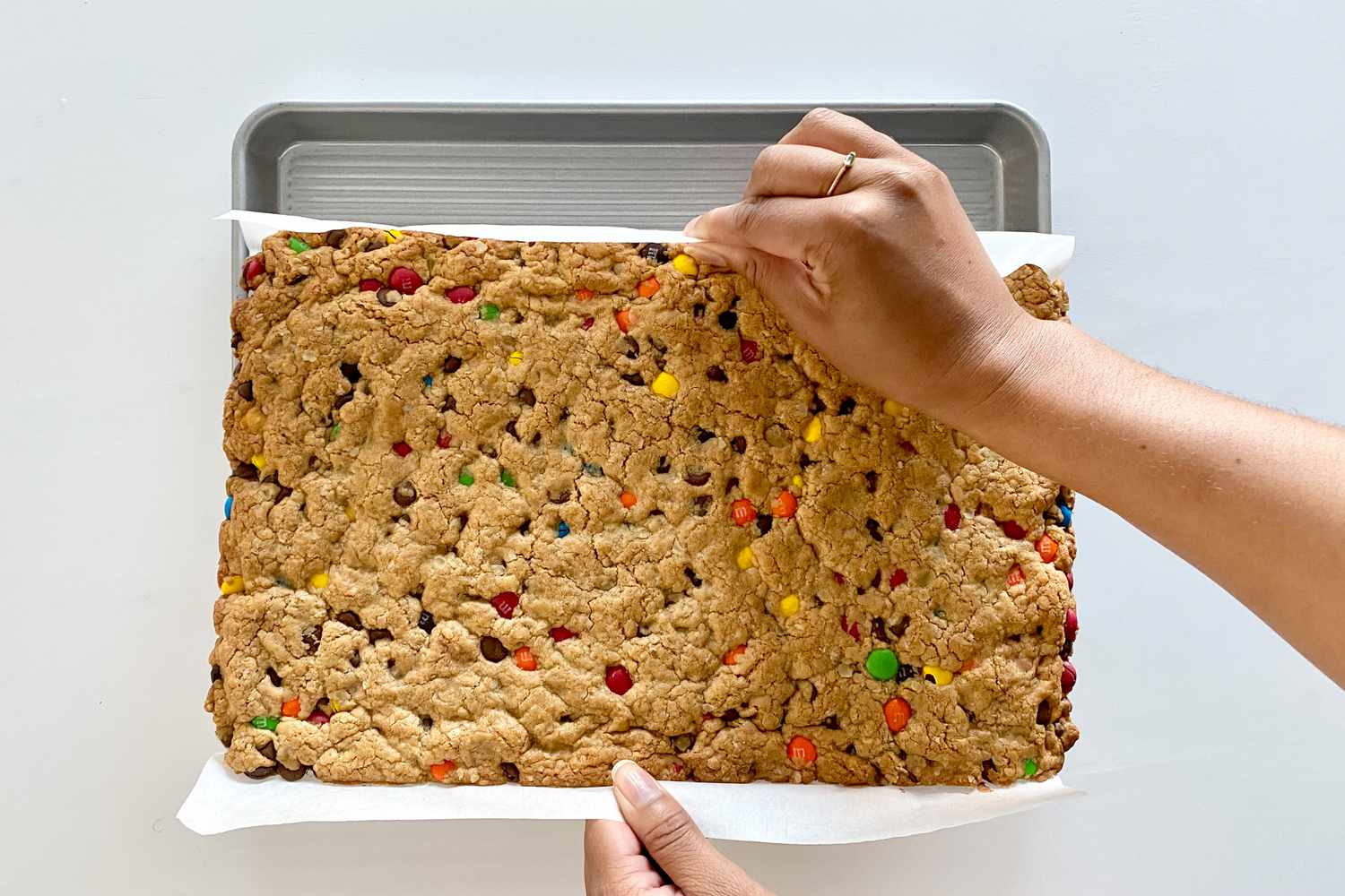 Removing Gluten-Free Sheet Pan Monster Cookies from the pan by holding the parchment.