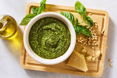 Bowl of basil pesto on a cutting board with fresh basil leaves pine nuts Parmesan cheese and olive oil