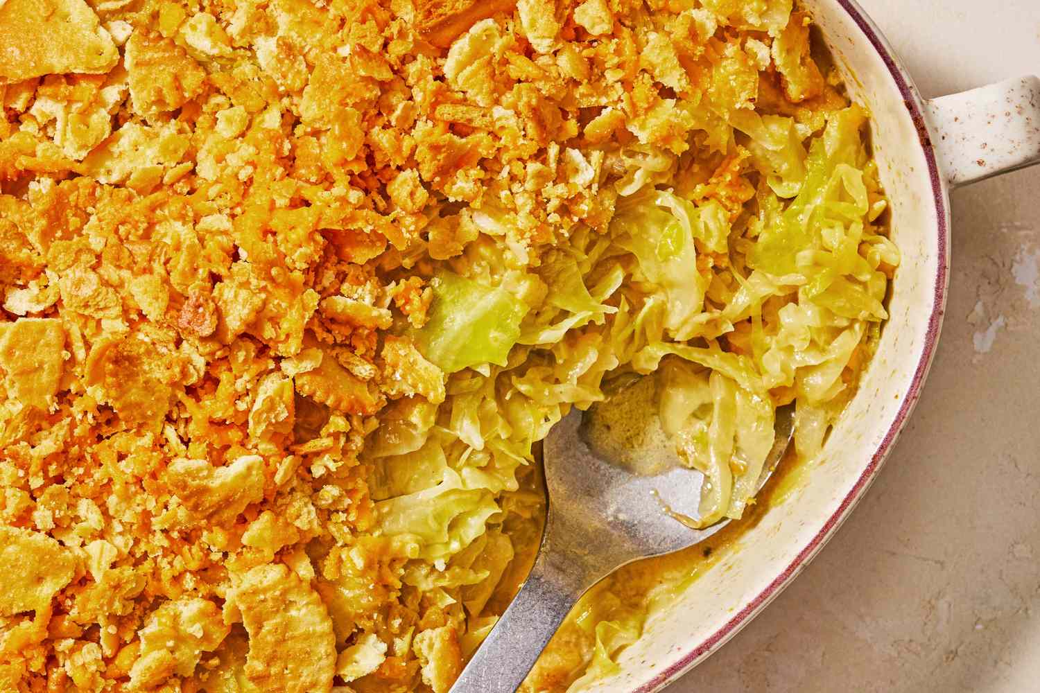 Cheesy cabbage casserole with a crunchy topping served in a baking dish with a serving spoon