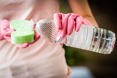 Person wearing gloves pouring liquid from a bottle onto a sponge