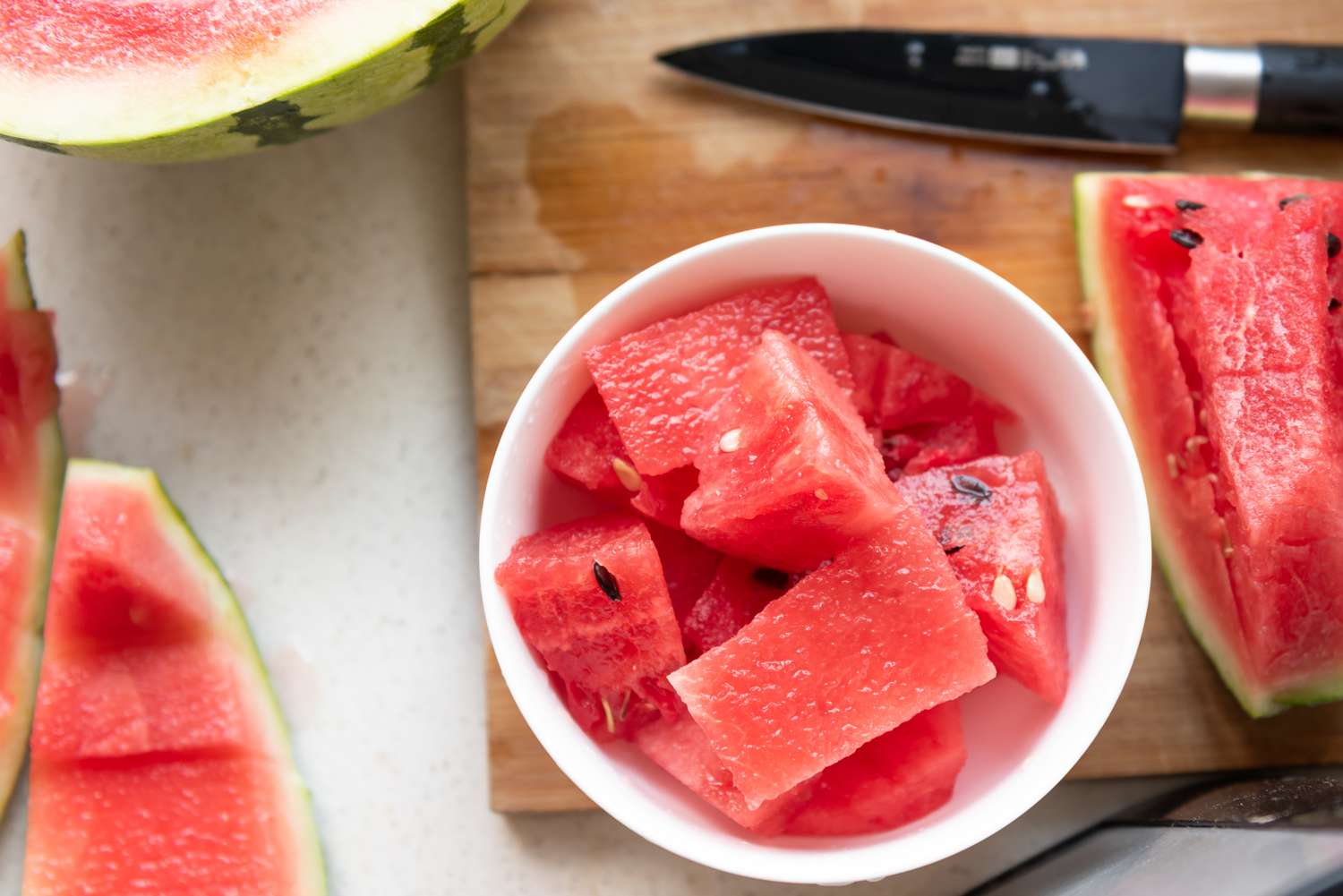 sliced watermelon in a bowl on a cutting board next to uncut watermelon wedge and watermelon rind on the counter