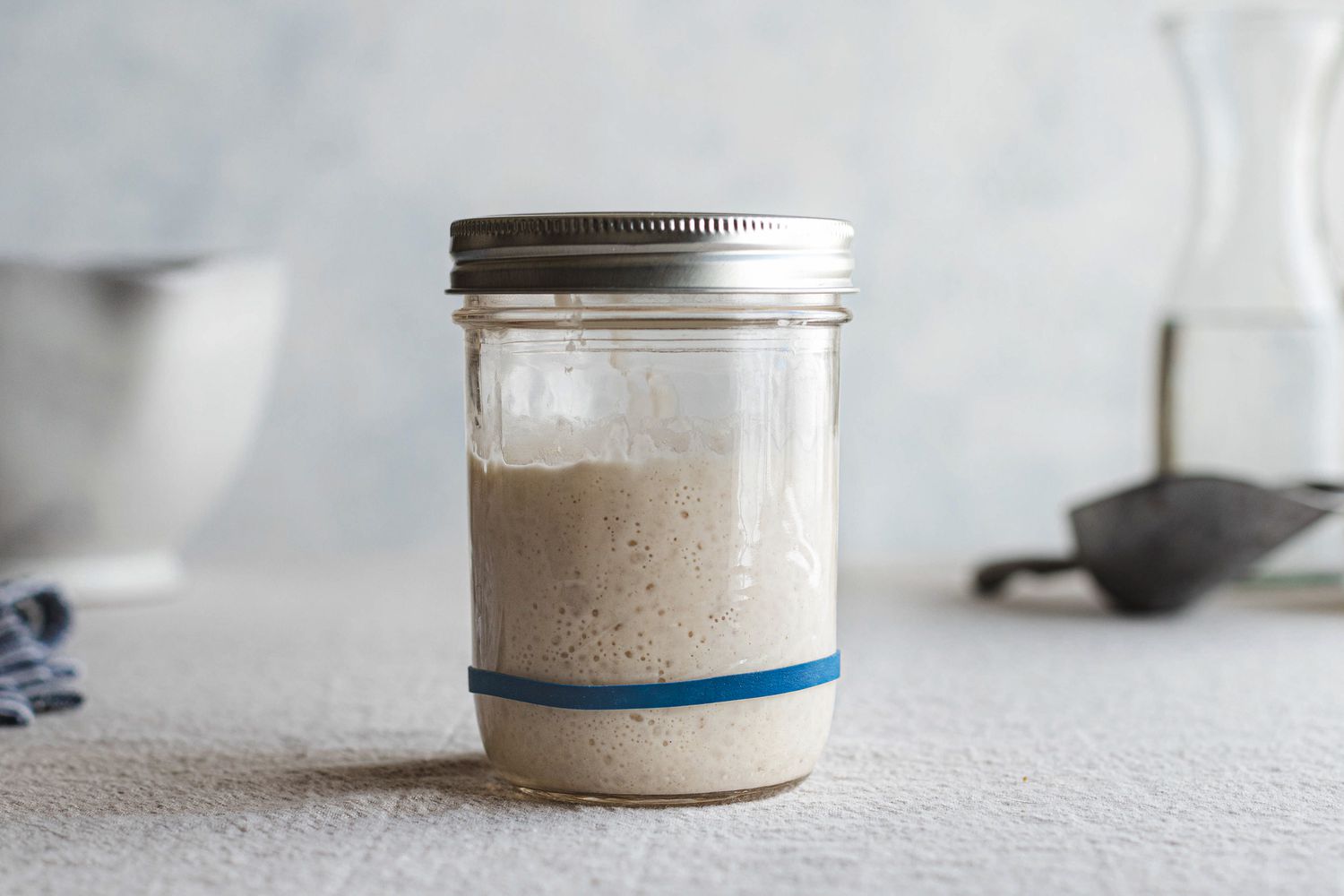 Side view of a mason jar with a rubberband around it and filled with a simple sourdough starter.