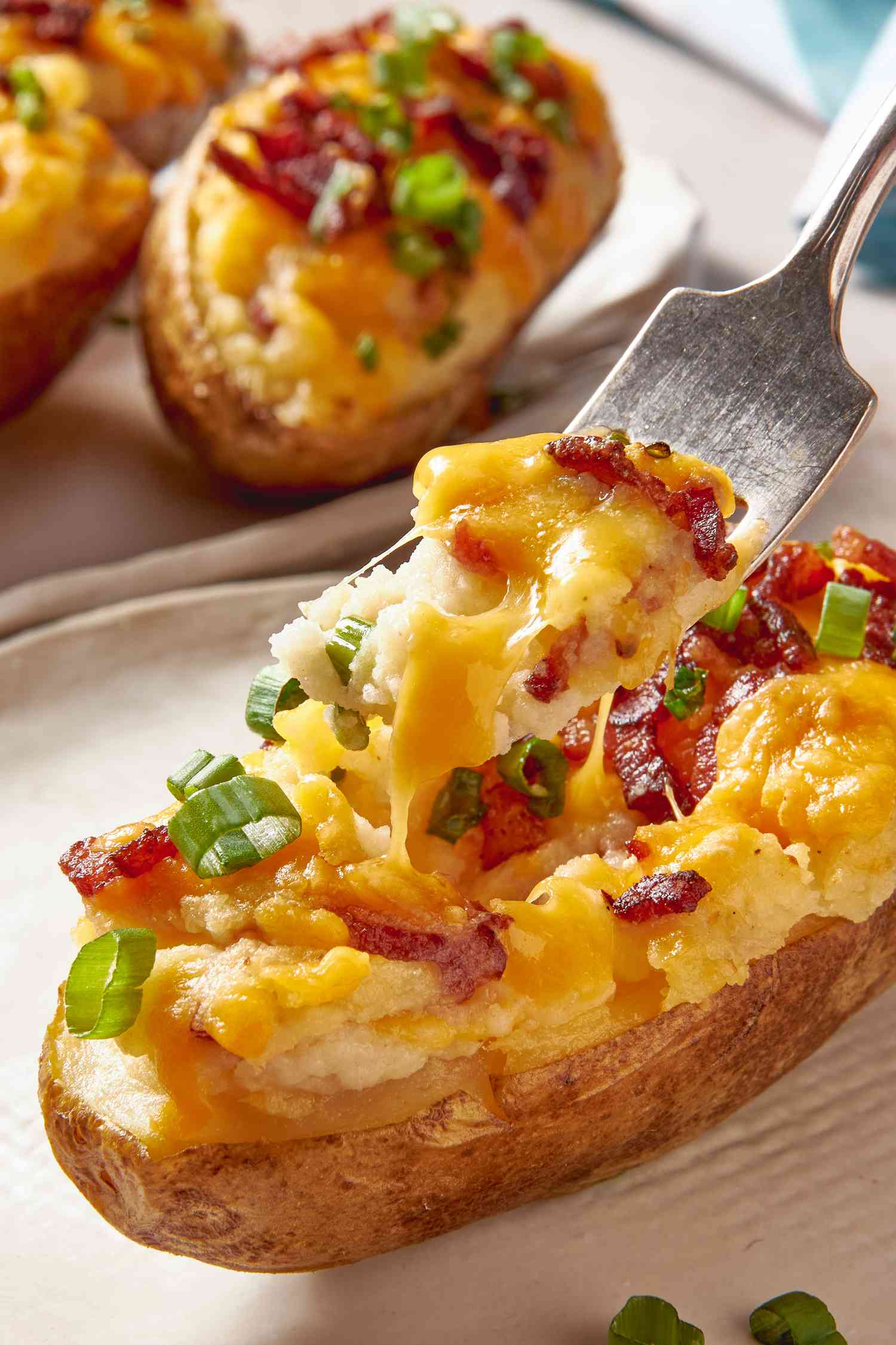 Fork lifting a bite-sized serving of twice baked potato up from a plate with the twice baked potato
