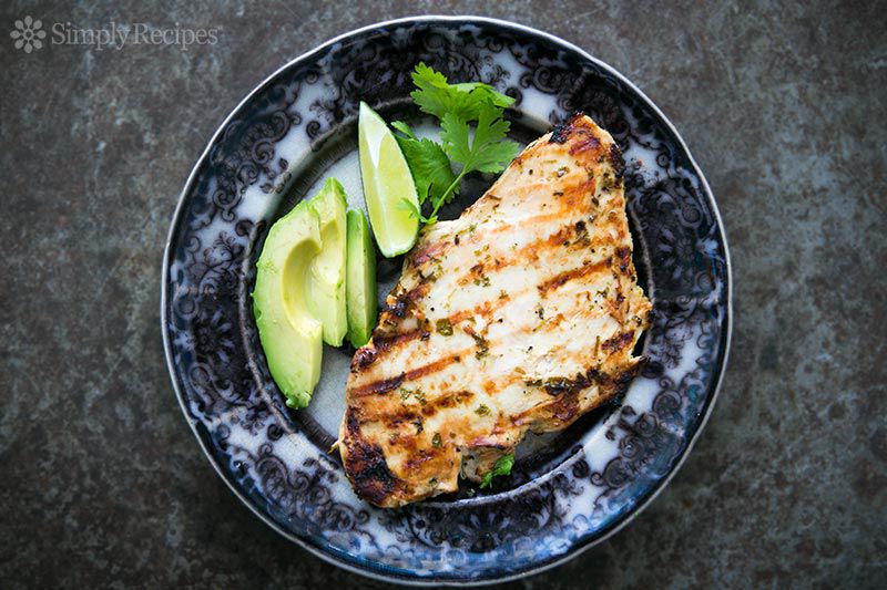 grilled chicken breast next to avocado slices, a lime wedge, and a sprig of cilantro