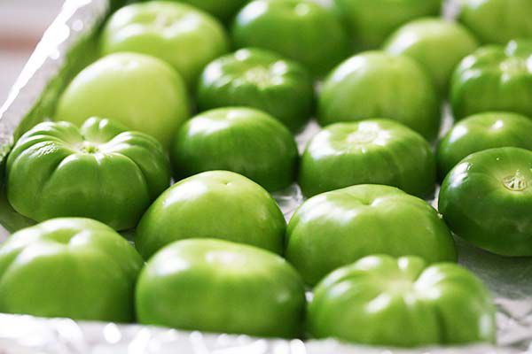 Tomatillos cut in half and resting cut-side down on a foiled baking sheet