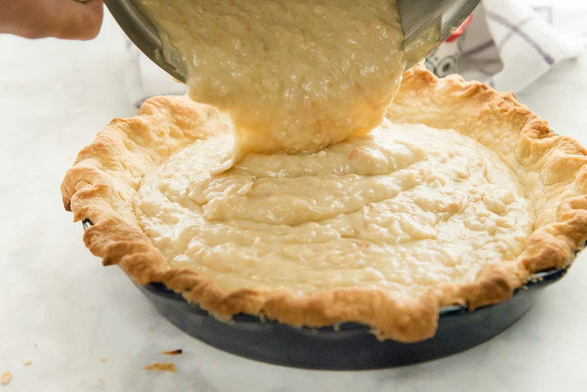 Coconut cream pie filling is being added to a baked pie crust for homemade coconut cream pie.
