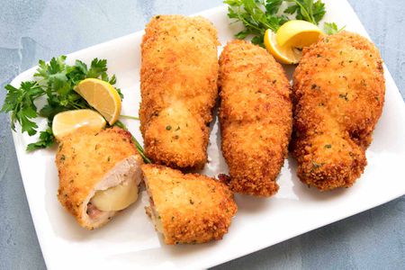 Homemade Chicken Cordon Bleu on a white platter with lemon wedges.