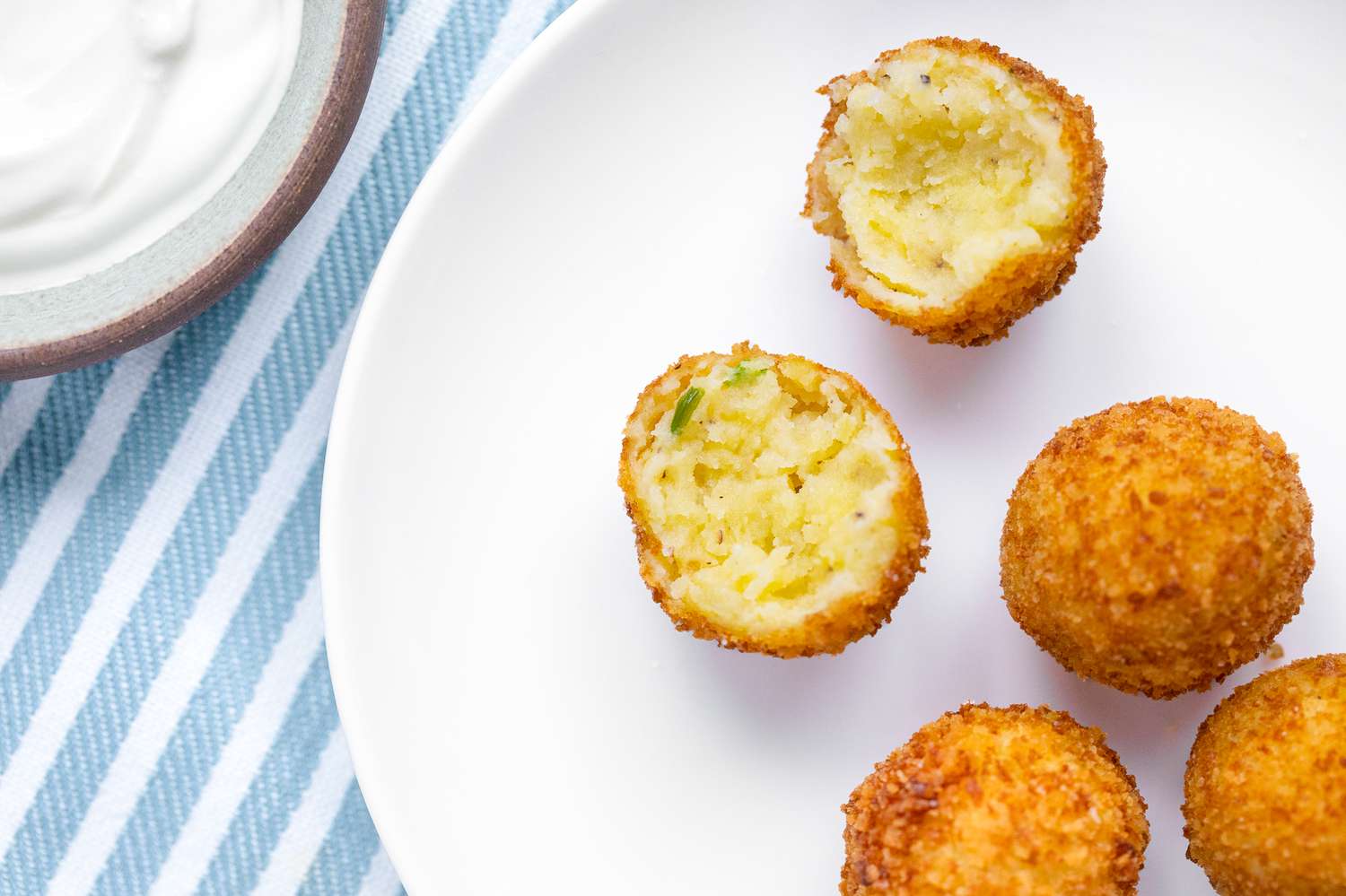 Potato Croquettes on a Plate with One Croquette Broken in Half, and Next to the Plate, a Small Saucer with Sauce
